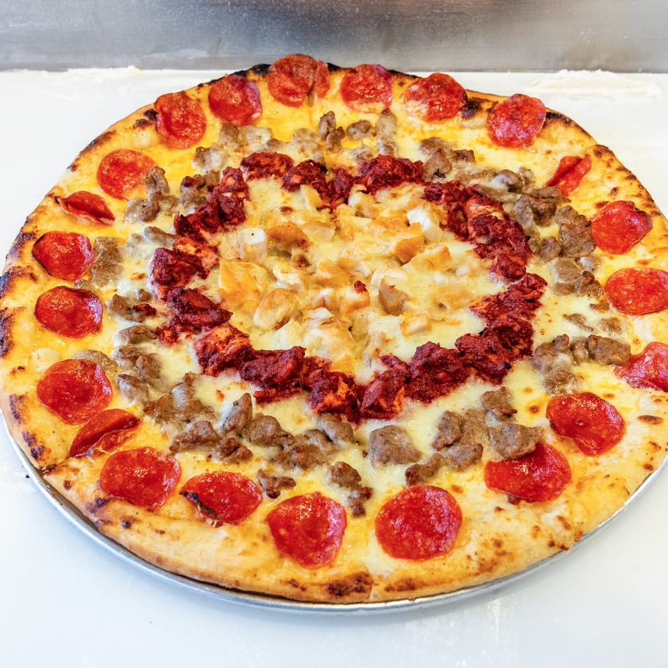 Large round pizza topped with pepperoni, sausage, crumbled meat, onions, and melted cheese on a metal tray.