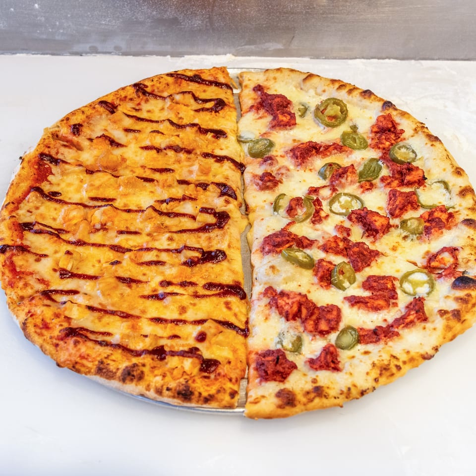 Two-sided pizza on a metal tray, topped with grilled cheese on one half and spicy sausage with jalapeños on the other.