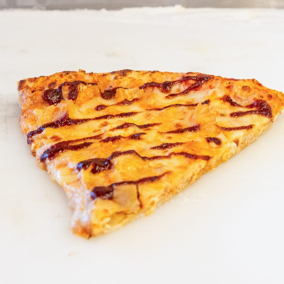 Triangular slice of golden baked pastry topped with melted cheese and dark sauce drizzles on a white surface.