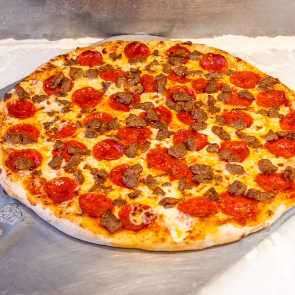 Large pepperoni and sausage pizza with melted cheese on a metal pizza peel.