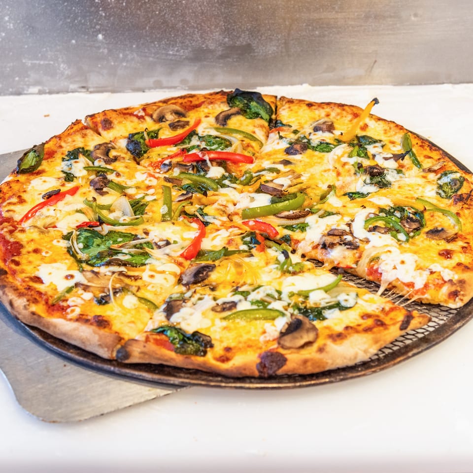 Large freshly baked vegetable pizza topped with mushrooms, peppers, spinach, onions, and melted cheese on a serving tray.